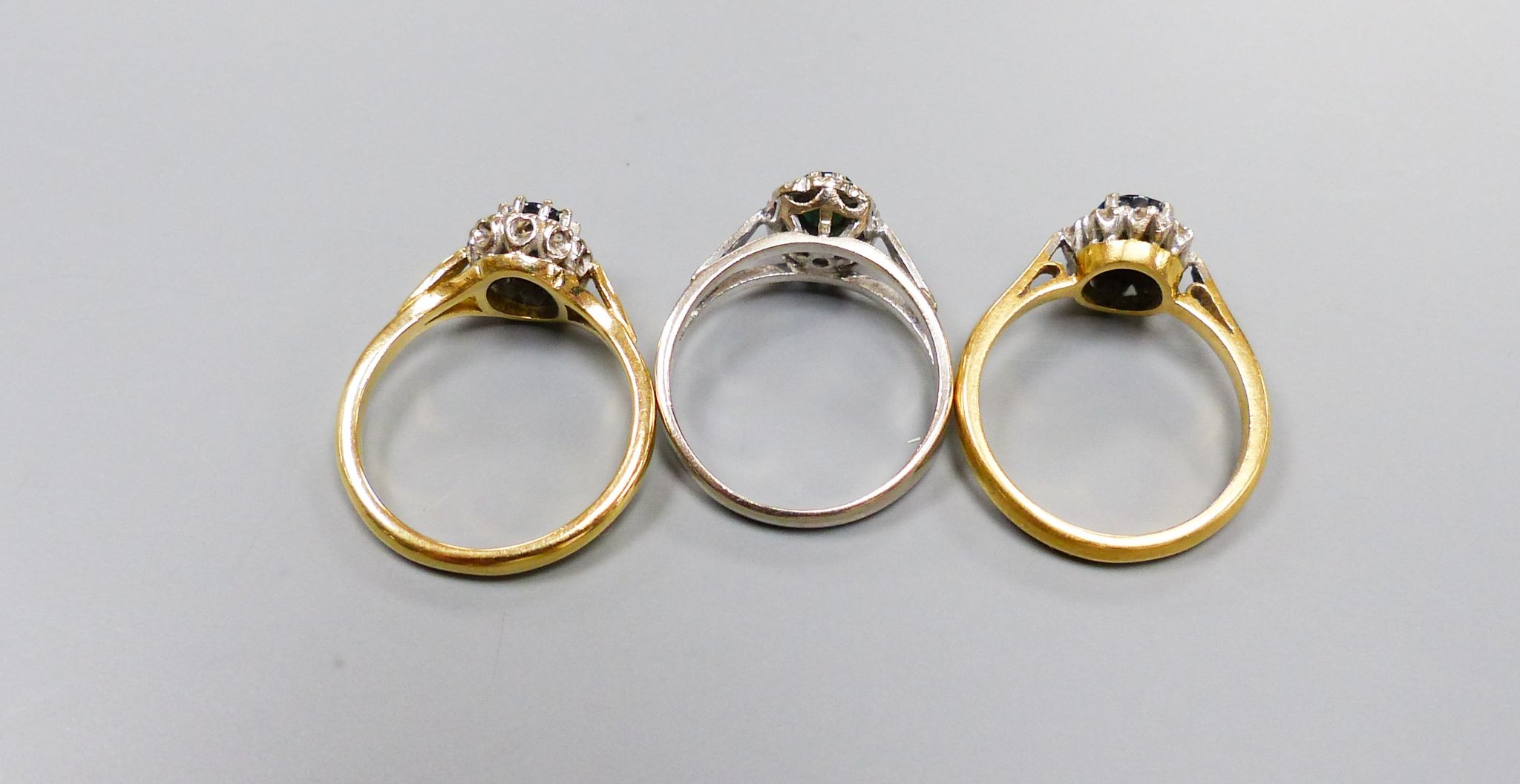 Three modern sapphire and diamond set oval cluster rings, including 18ct white gold, size M and 18ct, size L/M, (gross 7.2 grams and one yellow metal, size L/M, gross 3.8 grams.